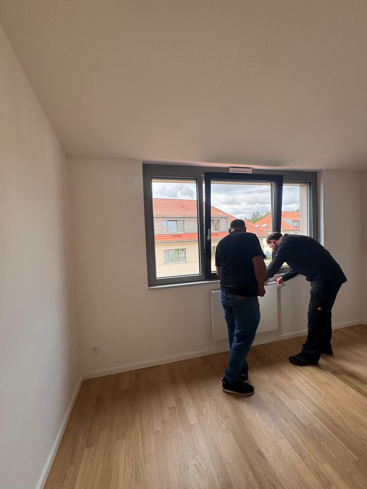 Zwei Mitarbeiter arbeiten am Fensterbereich eines hellen Raums mit Holzfußboden